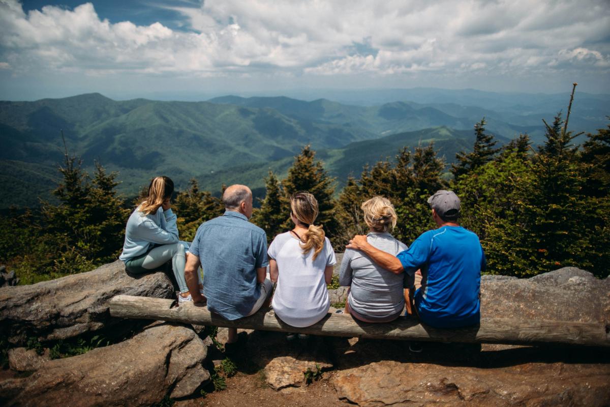 Family sitting on a log bench overlooking forested mountain ridges