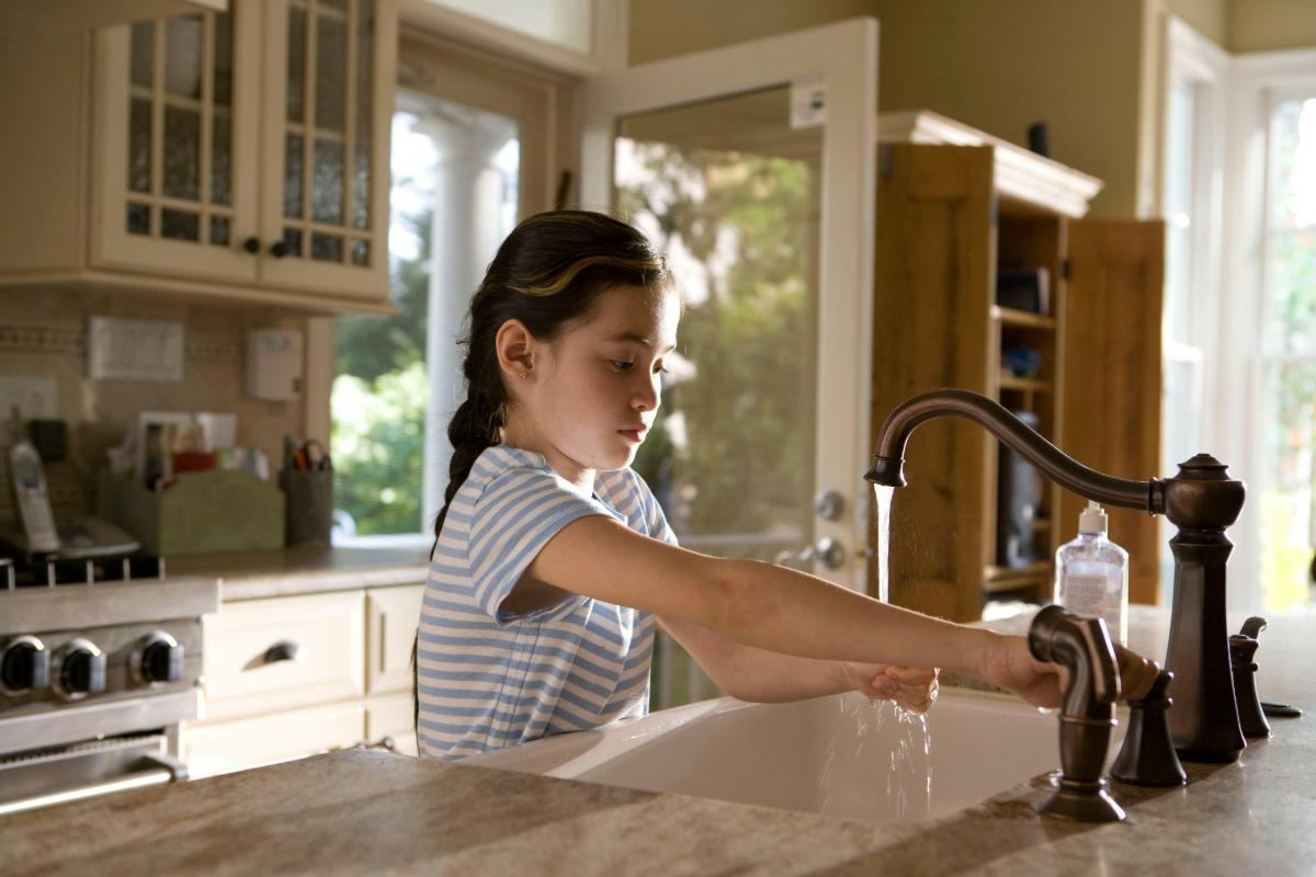 Child washing hands at a kitchen sink with steady running water